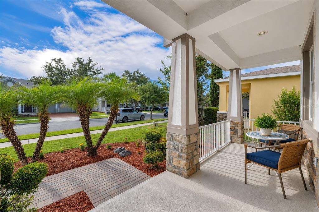 A covered front porch features stone-based columns, wicker furniture, and a view of the street — 9906 MOSS ROSE WAY, ORLANDO, FL