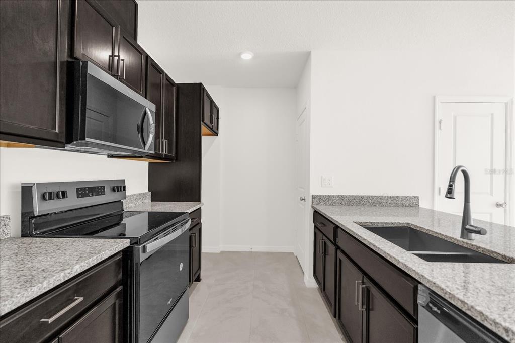 A kitchen features dark wood cabinets, granite countertops, stainless steel appliances, and light tile flooring — 399 SEQUOIA DRIVE, LAKE WALES, FL