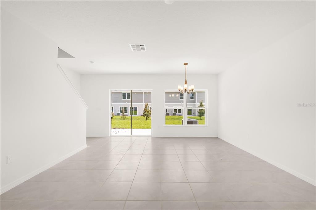 An empty room with white walls, light tile flooring, a chandelier, and sliding glass doors — 399 SEQUOIA DRIVE, LAKE WALES, FL