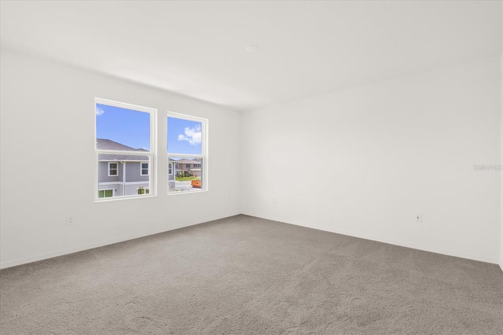 An empty bedroom features white walls, gray carpeting, and two windows overlooking neighboring houses — 399 SEQUOIA DRIVE, LAKE WALES, FL
