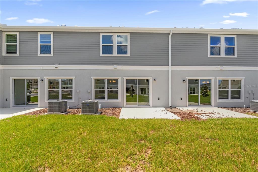 The exterior rear view of a multi-unit townhouse features gray siding, concrete patios, and air-conditioning units — 399 SEQUOIA DRIVE, LAKE WALES, FL