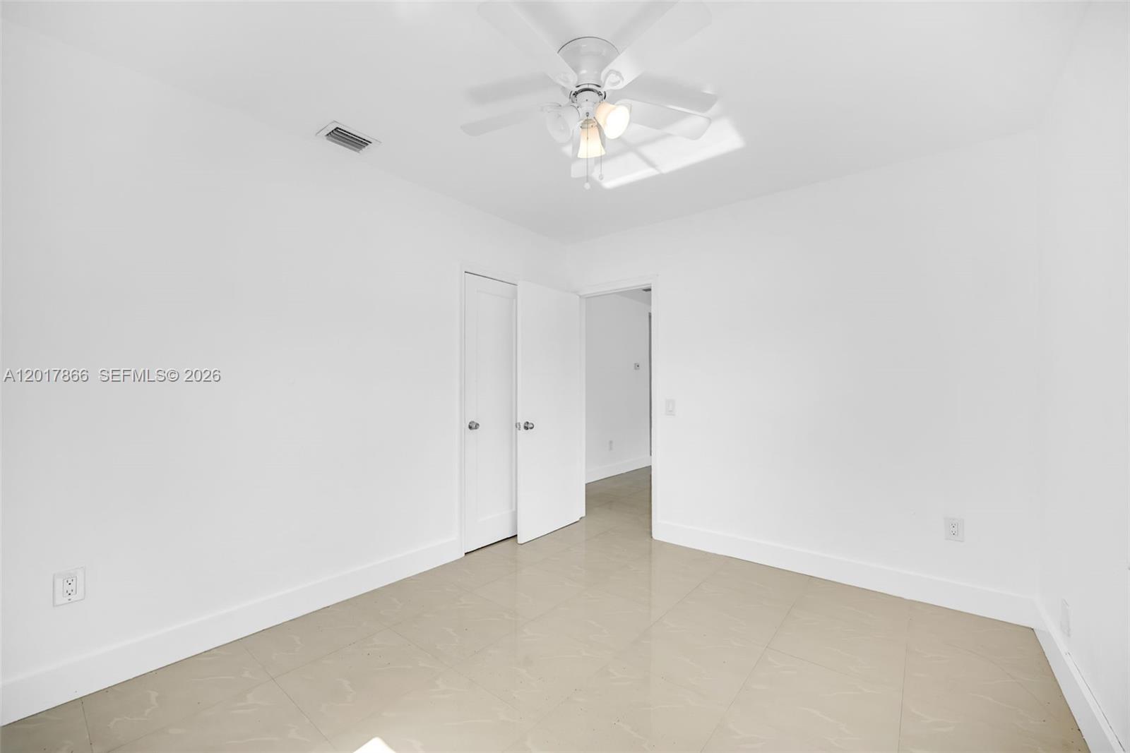 A bright, empty room features white walls, light-colored tile flooring, and a ceiling fan — 555 NW 90th St, El Portal FL 33150, EL PORTAL, FL