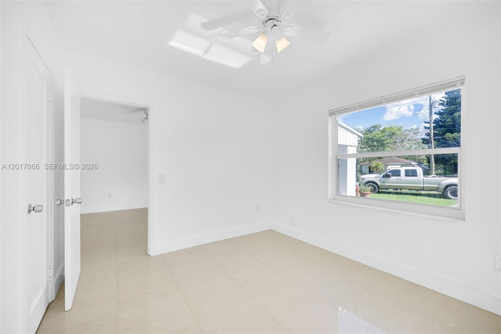 A bright, empty bedroom features white walls, tile flooring, a ceiling fan, and a window — 555 NW 90th St, El Portal FL 33150, EL PORTAL, FL