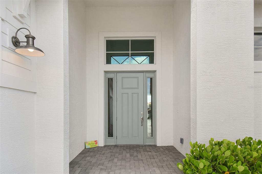 A light blue front door with sidelights and a transom window sits under a covered entryway — 8472 SW CANTANTE WAY, PORT ST LUCIE, FL