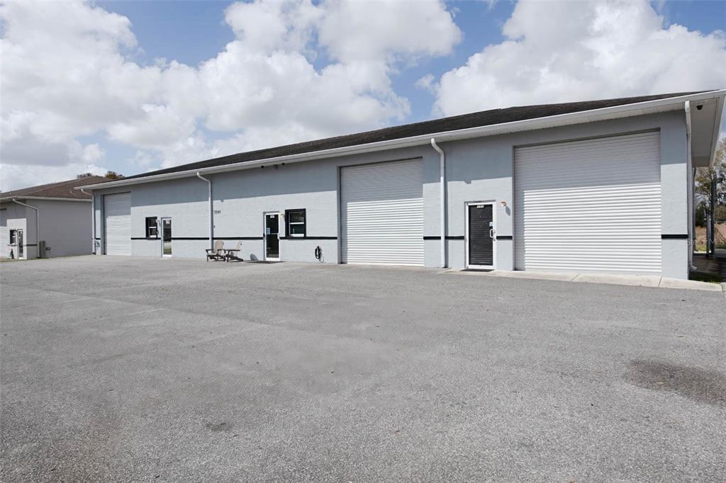 A gray commercial building features multiple roll-up doors and glass entry doors on a paved lot — 3398 SW 74TH AVENUE, OCALA, FL