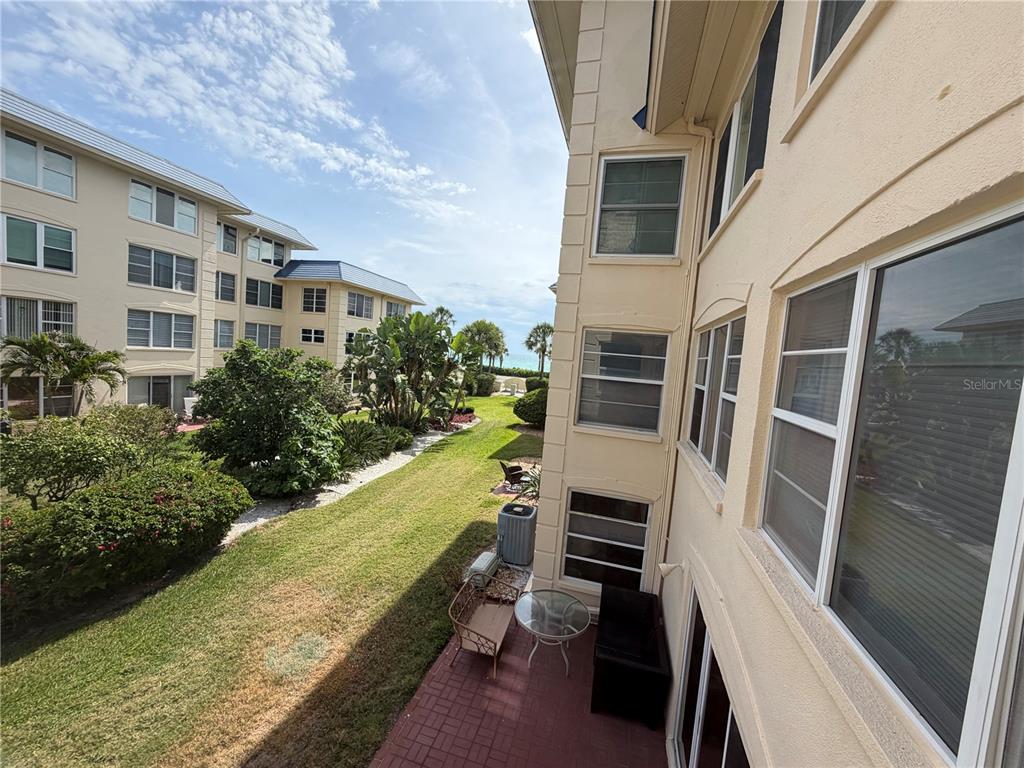 An outdoor patio with furniture overlooks a grassy courtyard between two multi-story apartment buildings — 3802 GULF OF MEXICO DRIVE UNIT A204, LONGBOAT KEY, FL