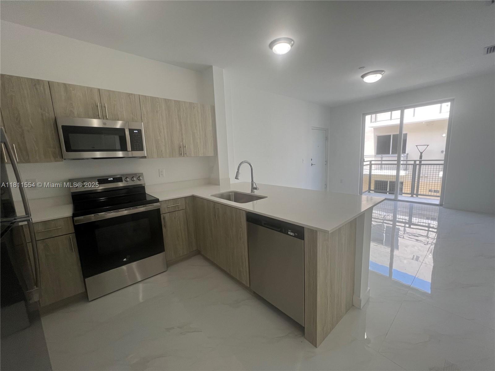 A modern kitchen features light wood cabinets, stainless steel appliances, and white marble-look tile flooring — 1010 SW 69th Ave # 212, Miami FL 33144, MIAMI, FL