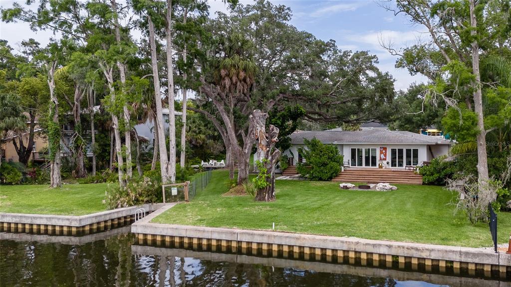 A waterfront house with a large lawn, mature trees, and a concrete bulkhead — 7308 N OLA AVENUE, TAMPA, FL