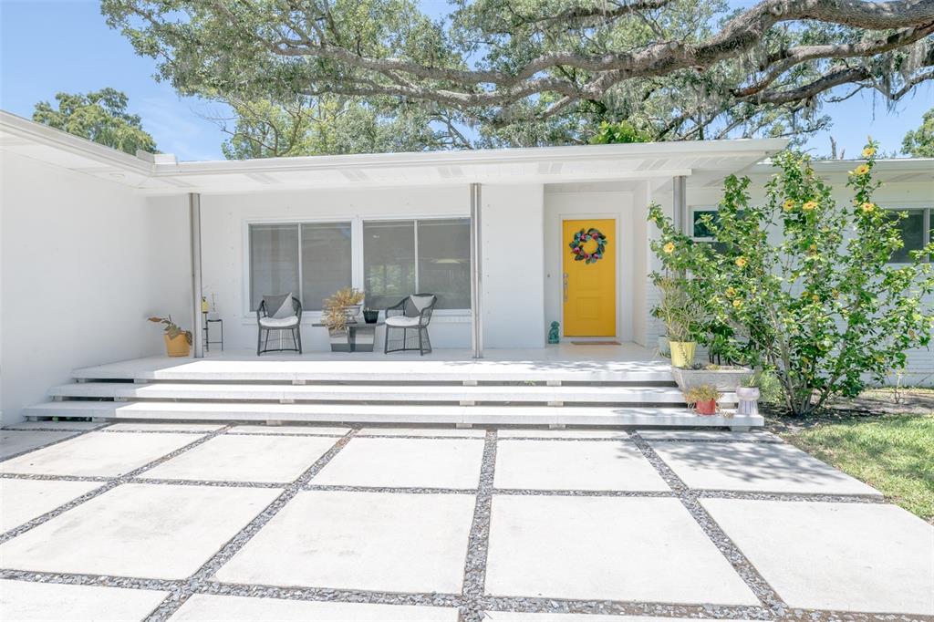 A white mid-century modern house features a bright yellow door and a tiered front porch — 7308 N OLA AVENUE, TAMPA, FL
