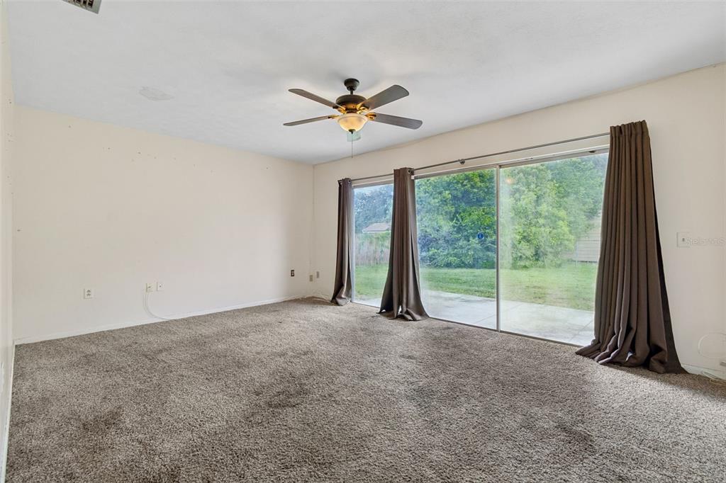 An empty living room features beige walls, brown carpeting, a ceiling fan, and sliding glass doors — 418 DEWOLF ROAD, BRANDON, FL