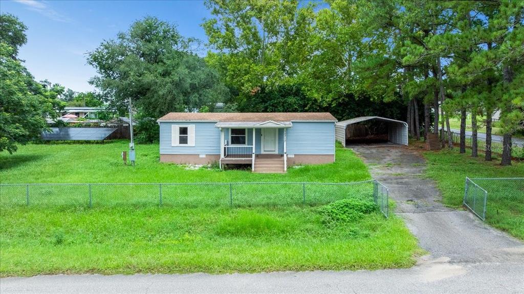 A light blue single-story house with a front porch, metal carport, and chain-link fence — 10717 SE 129TH STREET, BELLEVIEW, FL
