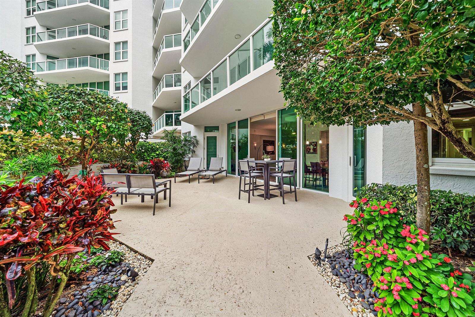 A ground-floor patio with outdoor furniture, lush landscaping, and a view of a high-rise building — 550 SE Mizner Boulevard # B110, Boca Raton FL 33432, BOCA RATON, FL