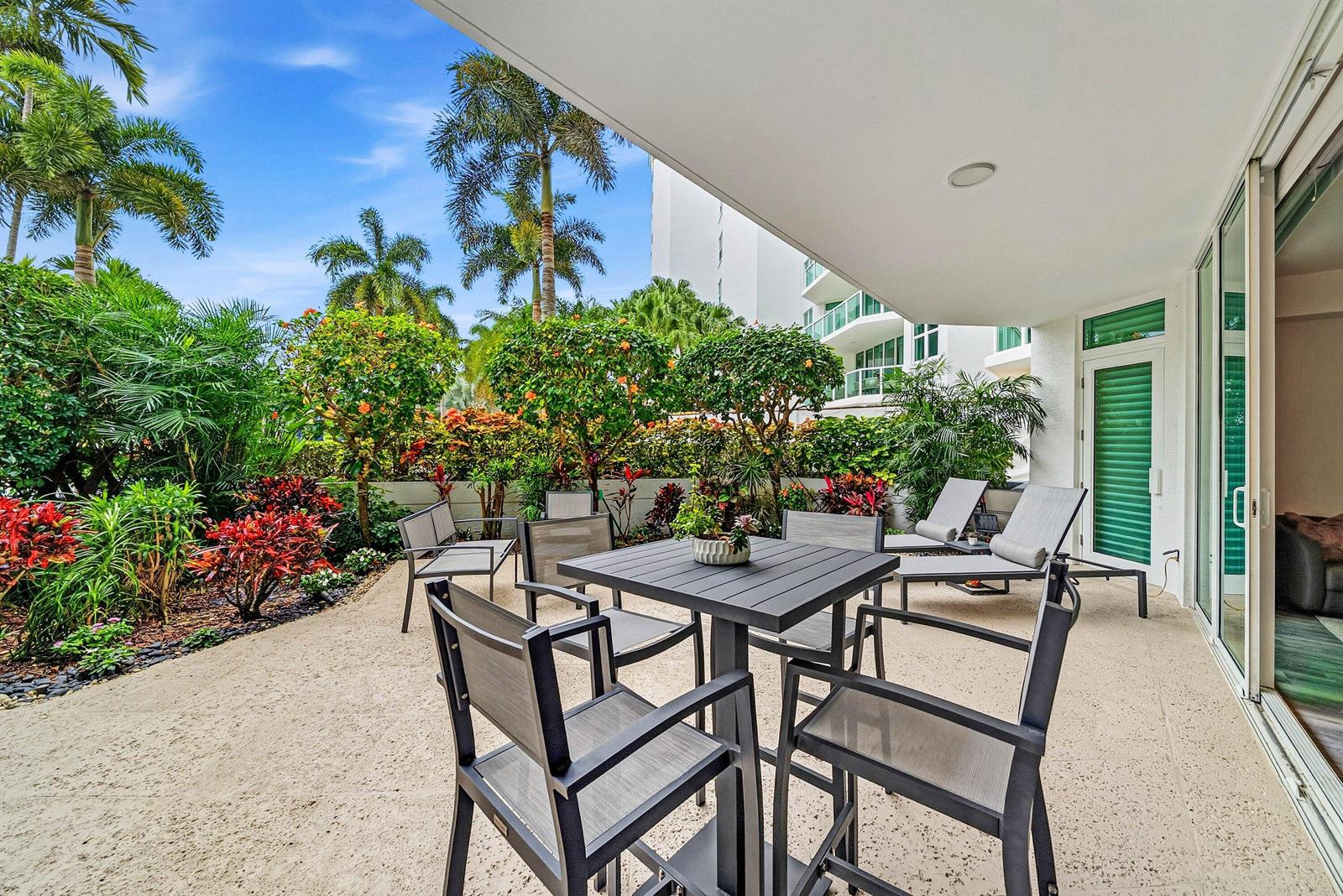 A patio with a dining set and lounge chairs overlooks a lush tropical garden — 550 SE Mizner Boulevard # B110, Boca Raton FL 33432, BOCA RATON, FL