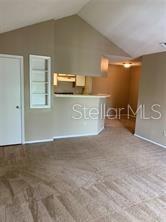 A carpeted living room features a vaulted ceiling, a white door, and a kitchen breakfast bar — 236 AFTON SQUARE UNIT 306, ALTAMONTE SPRINGS, FL