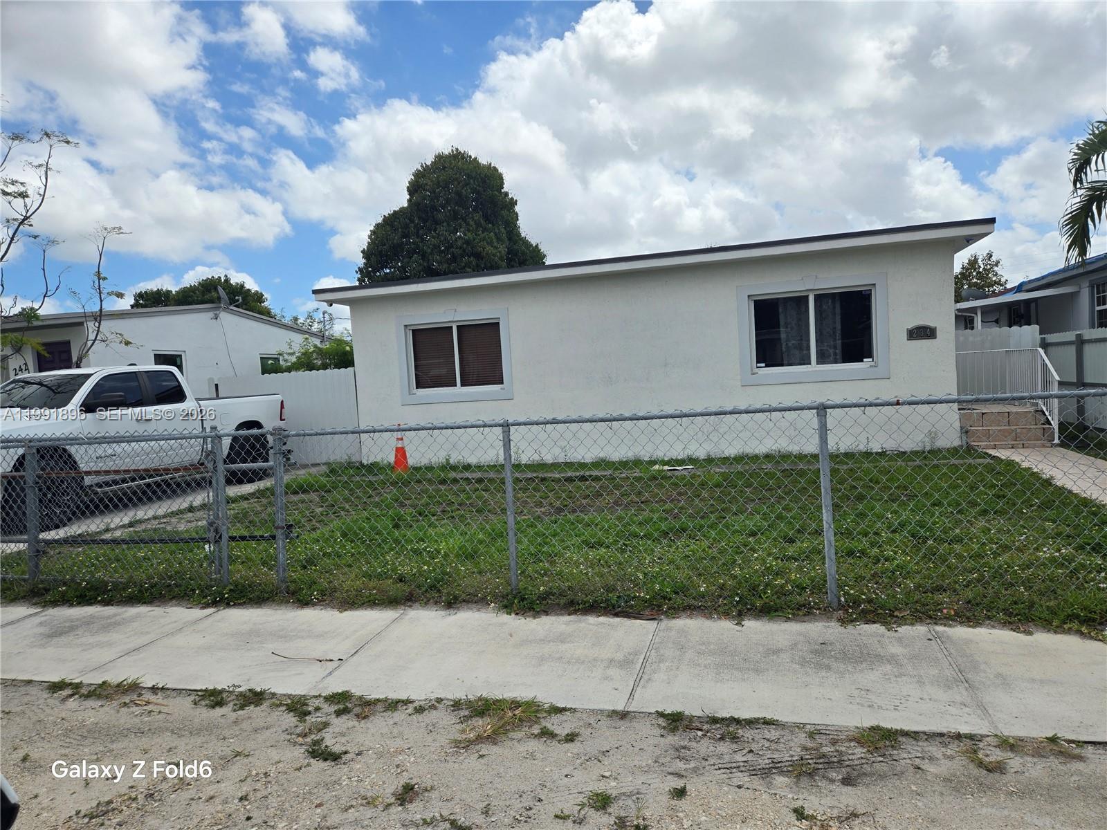 A white single-story house with a chain-link fence and a parked truck in front — 234 E 44th St, Hialeah FL 33013, HIALEAH, FL
