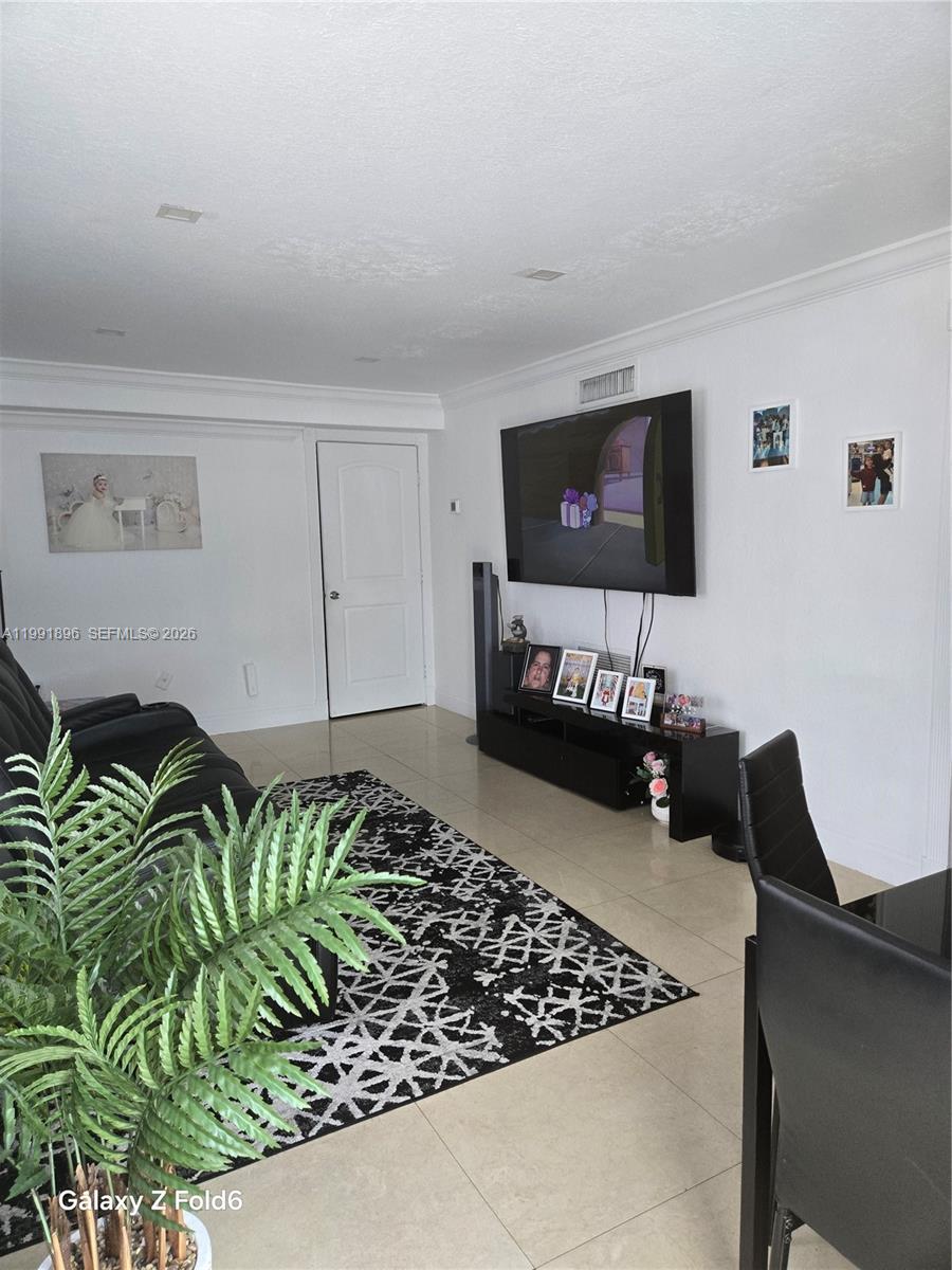 A living room features a black sofa, a patterned rug, and a wall-mounted television — 234 E 44th St, Hialeah FL 33013, HIALEAH, FL