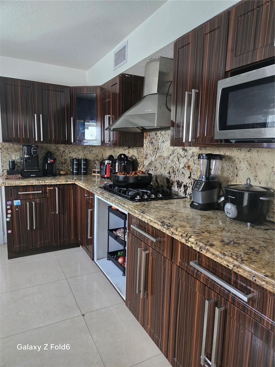 A kitchen features dark wood-grain cabinets, granite countertops, and stainless steel appliances — 234 E 44th St, Hialeah FL 33013, HIALEAH, FL
