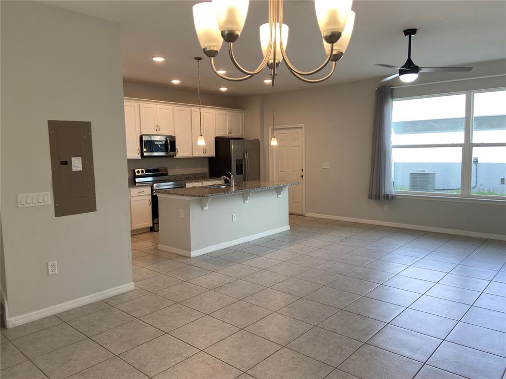 A kitchen with white cabinets, granite countertops, and a center island opens to a living area — 5029 AVALON PARK BOULEVARD, WESLEY CHAPEL, FL