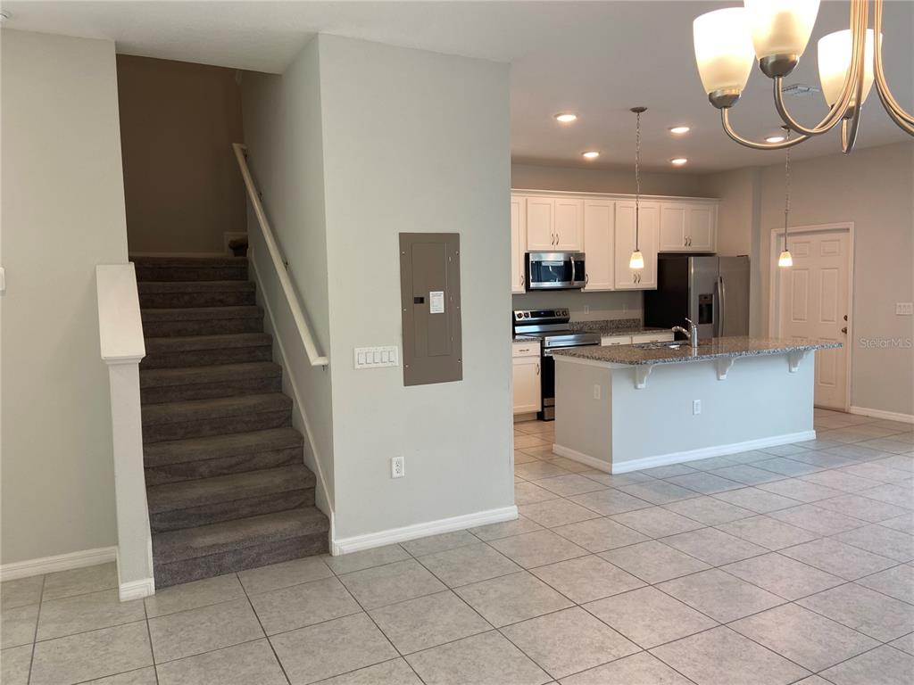 A carpeted staircase sits beside an open kitchen featuring white cabinets and a granite island — 5029 AVALON PARK BOULEVARD, WESLEY CHAPEL, FL