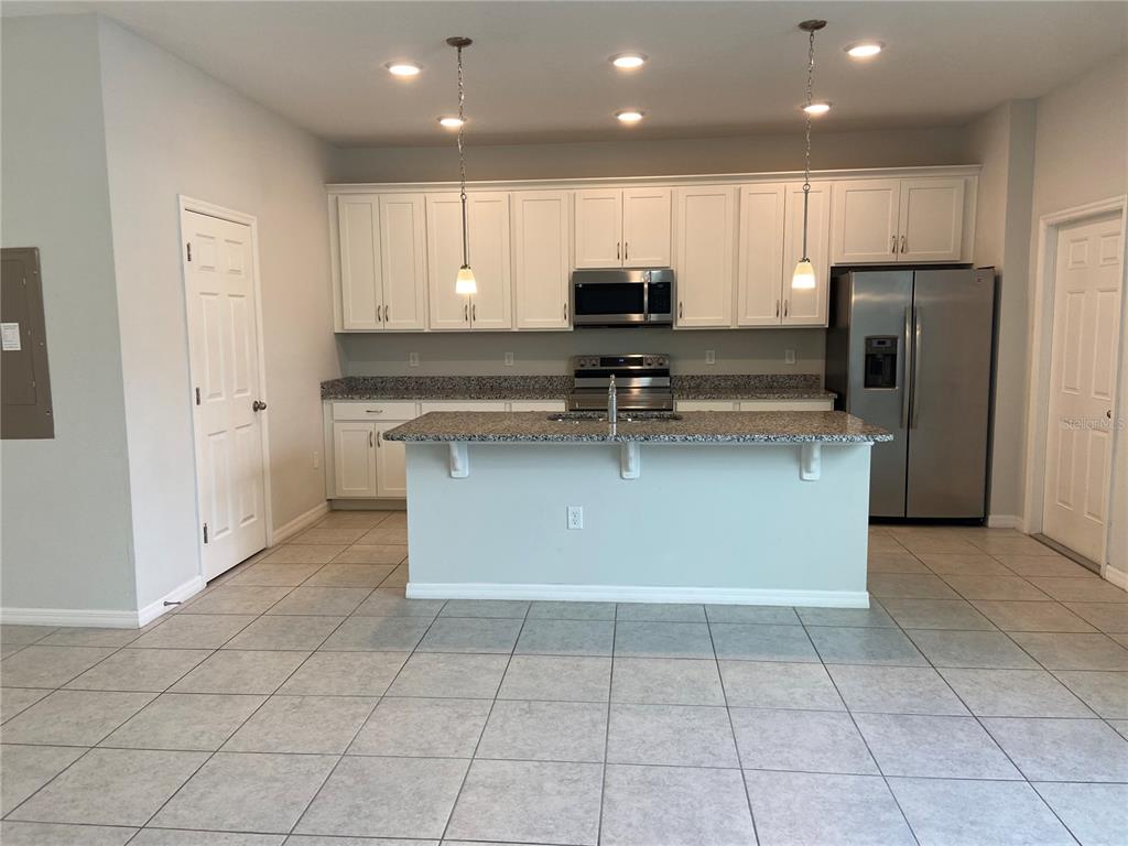 A kitchen features white cabinets, granite countertops, a center island, and stainless steel appliances — 5029 AVALON PARK BOULEVARD, WESLEY CHAPEL, FL