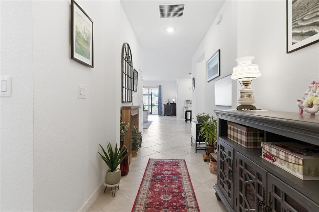A long, tiled hallway features a red runner rug, a console table, and wall art — 19060 CABERNET COURT, VENICE, FL