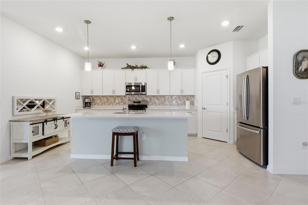 A kitchen features white cabinets, a central island with a stool, and stainless steel appliances — 19060 CABERNET COURT, VENICE, FL