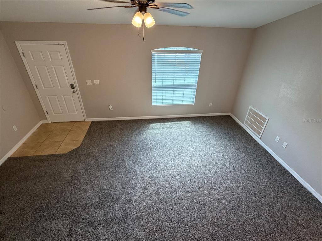 An empty room features gray carpet, a tiled entryway, a ceiling fan, and one window — 15369 SW 65TH TERRACE ROAD, OCALA, FL