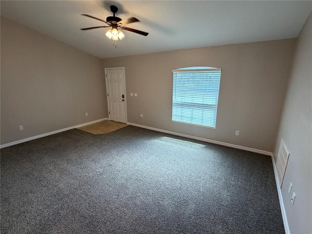 An empty room with gray carpet, beige walls, a ceiling fan, and a single window — 15369 SW 65TH TERRACE ROAD, OCALA, FL