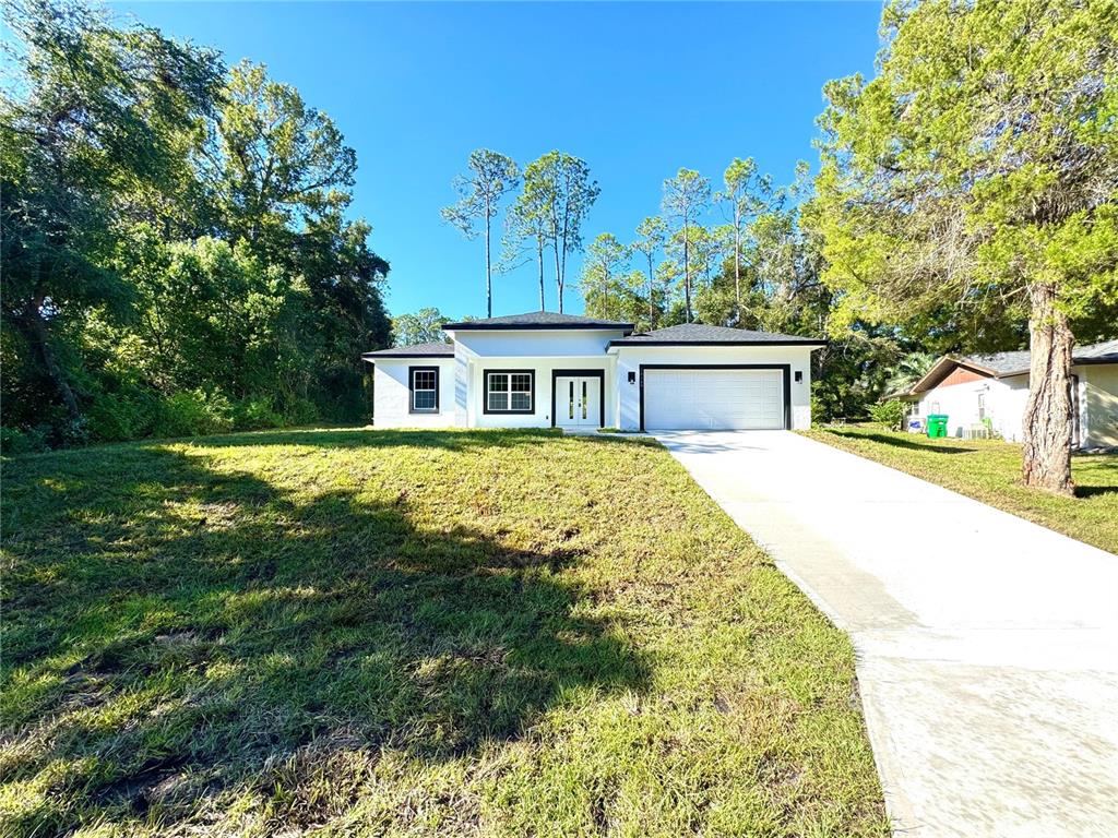 A white single-story house with a two-car garage sits on a grassy lot — 10160 N ACADEMY DRIVE, CITRUS SPRINGS, FL