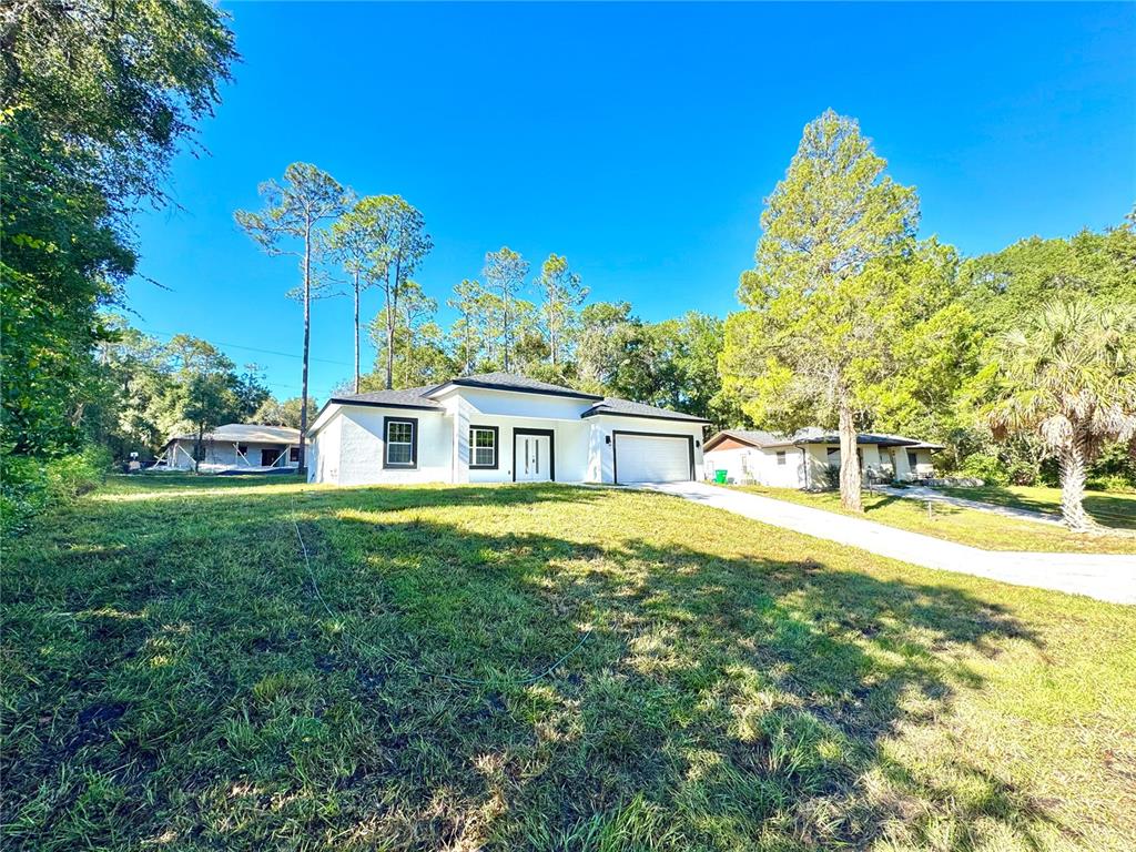 A white, single-story house with a garage sits on a grassy lot among trees — 10160 N ACADEMY DRIVE, CITRUS SPRINGS, FL