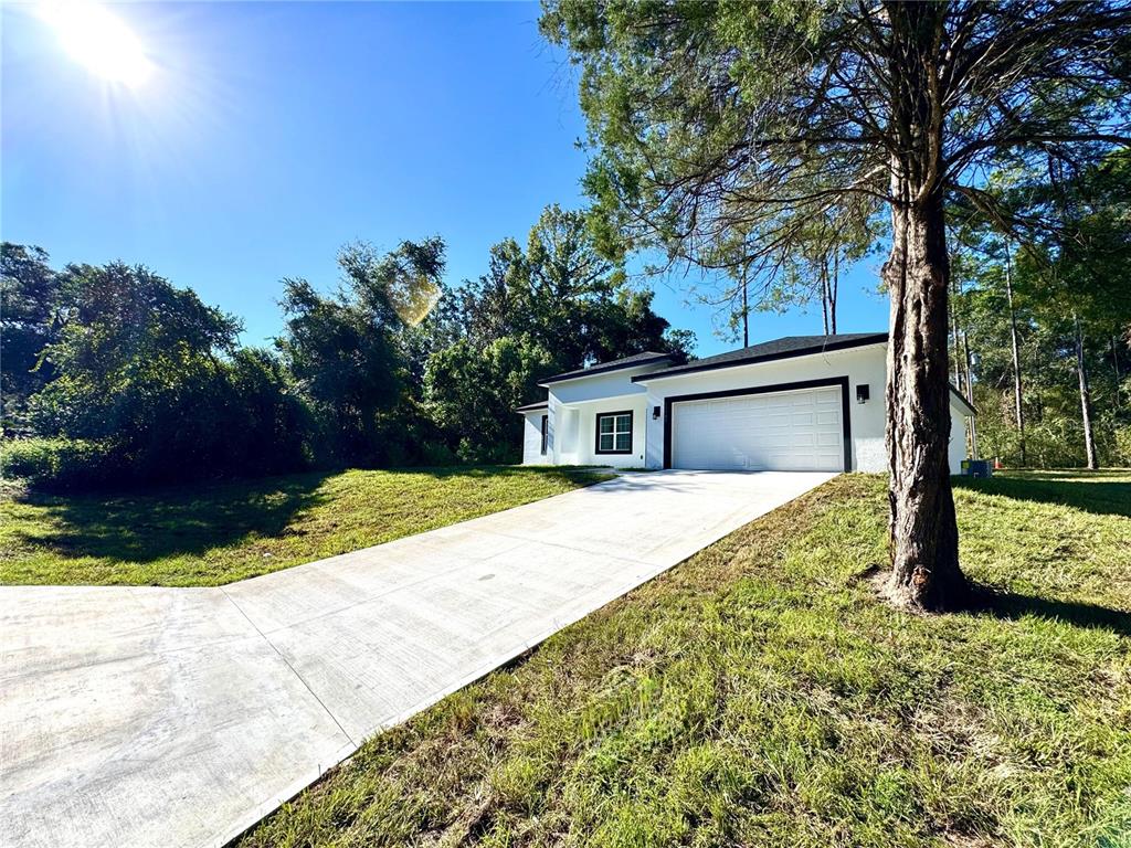A white house with a black-trimmed garage and windows sits at the end of a driveway — 10160 N ACADEMY DRIVE, CITRUS SPRINGS, FL