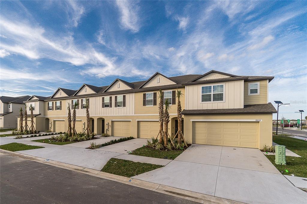 A row of modern two-story townhouses features beige siding, attached garages, and small palm trees — 32123 POND APPLE BEND, SAN ANTONIO, FL