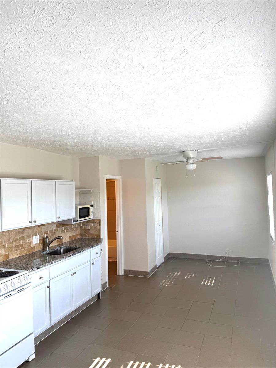 A kitchen with white cabinets, a tiled backsplash, and gray flooring opens to a dining area — 605 N Federal Highway # 14, FL 33460, FL