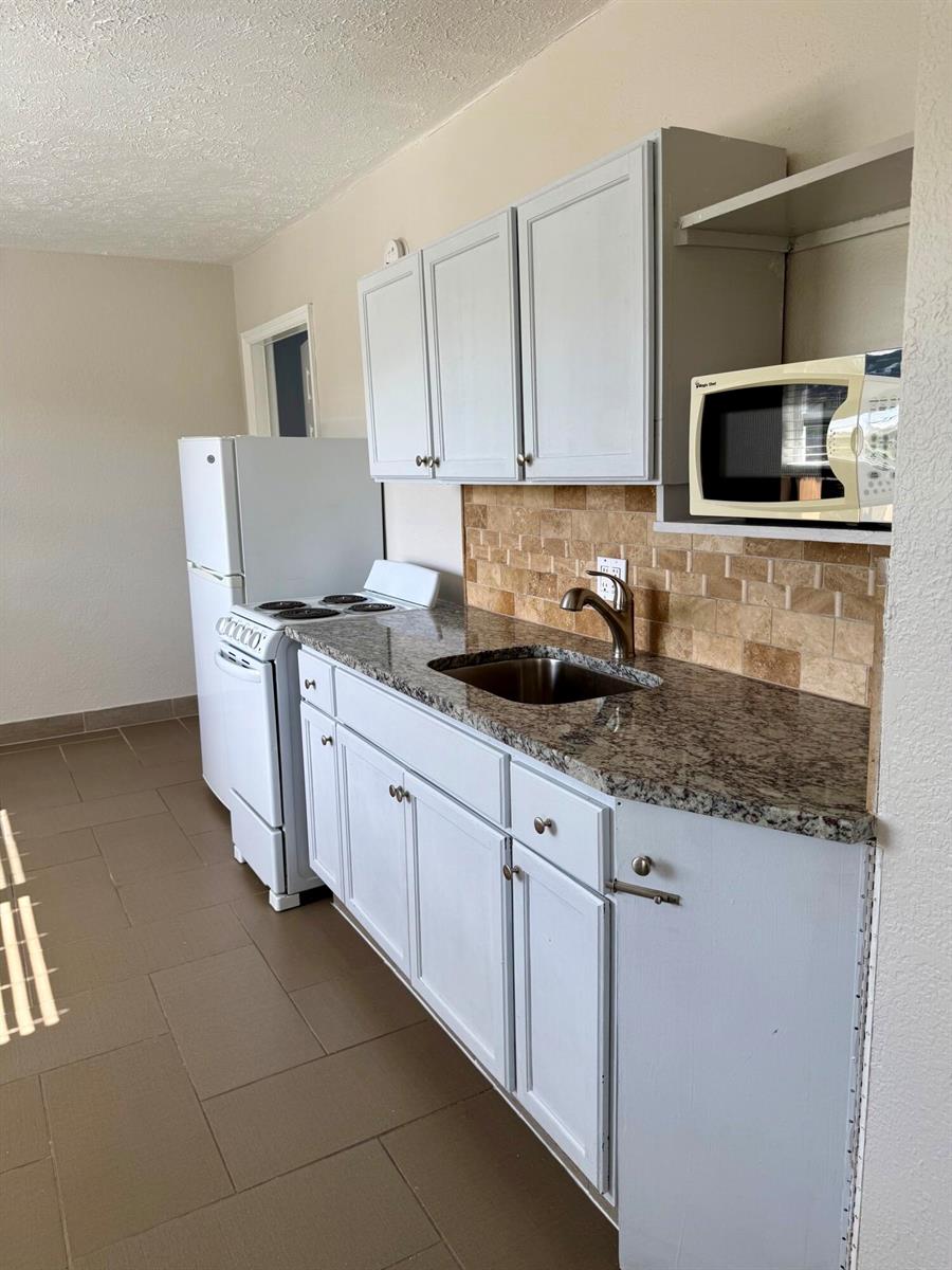 A kitchen features white cabinets, granite countertops, a stainless steel sink, and a white stove — 605 N Federal Highway # 14, FL 33460, FL