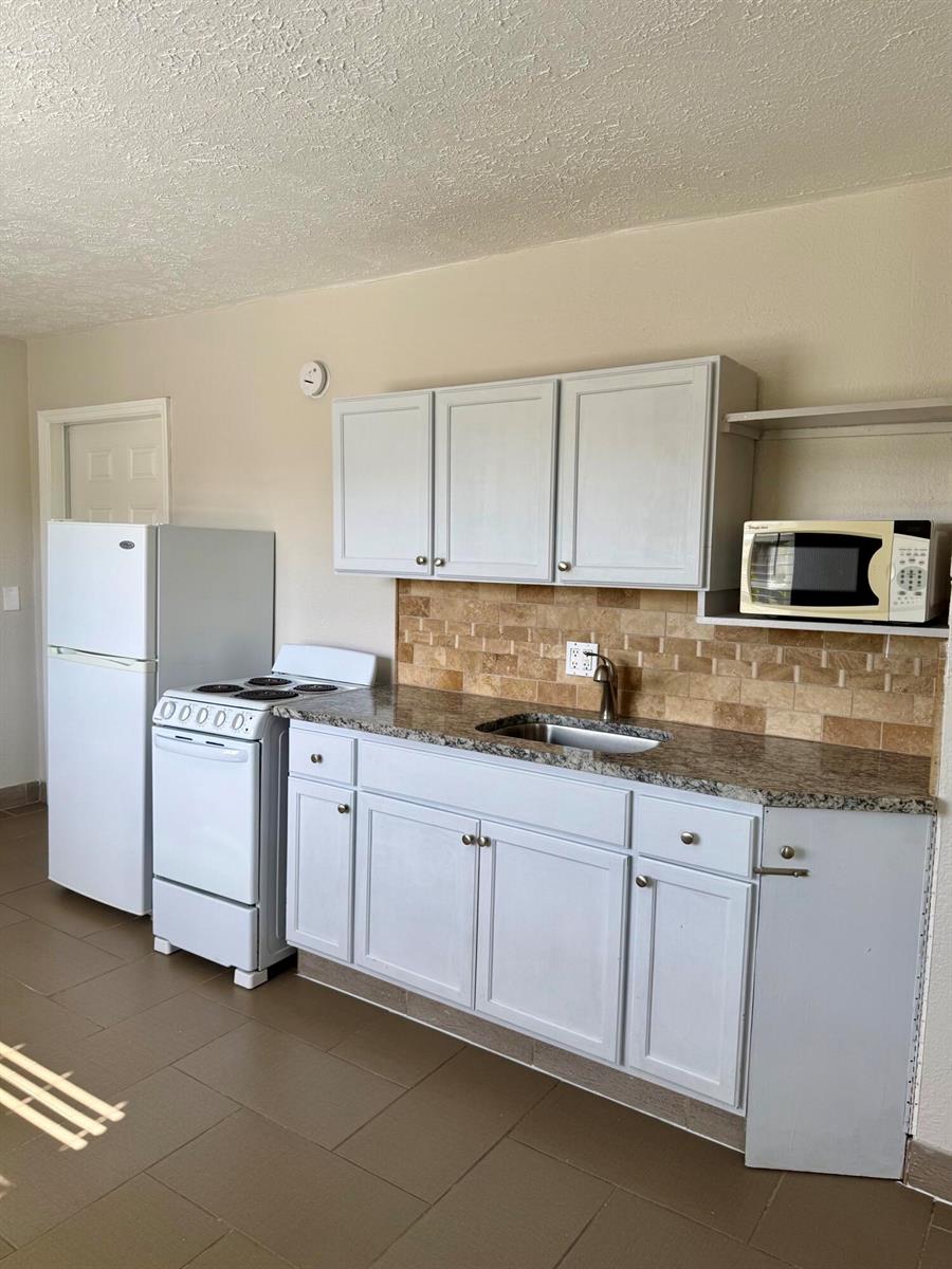 A kitchen features white cabinets, granite countertops, a tiled backsplash, and white appliances — 605 N Federal Highway # 14, FL 33460, FL