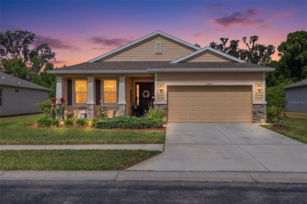 A single-story tan house with a two-car garage and stone accents sits under a sunset — 12421 EASTPOINTE DRIVE, DADE CITY, FL