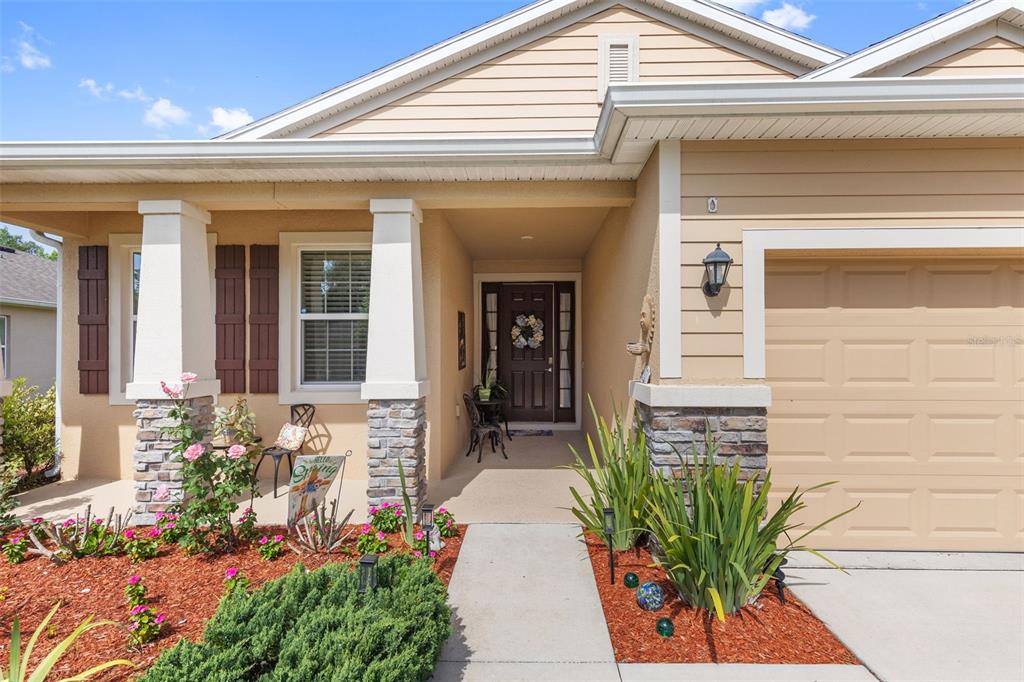 The exterior of a tan house features a stone-accented porch, a garage, and landscaping — 12421 EASTPOINTE DRIVE, DADE CITY, FL
