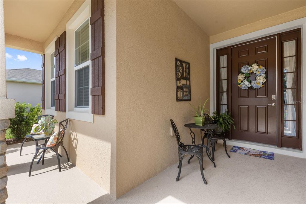 A covered front porch features a brown door with sidelights, two bistro sets, and shutters — 12421 EASTPOINTE DRIVE, DADE CITY, FL