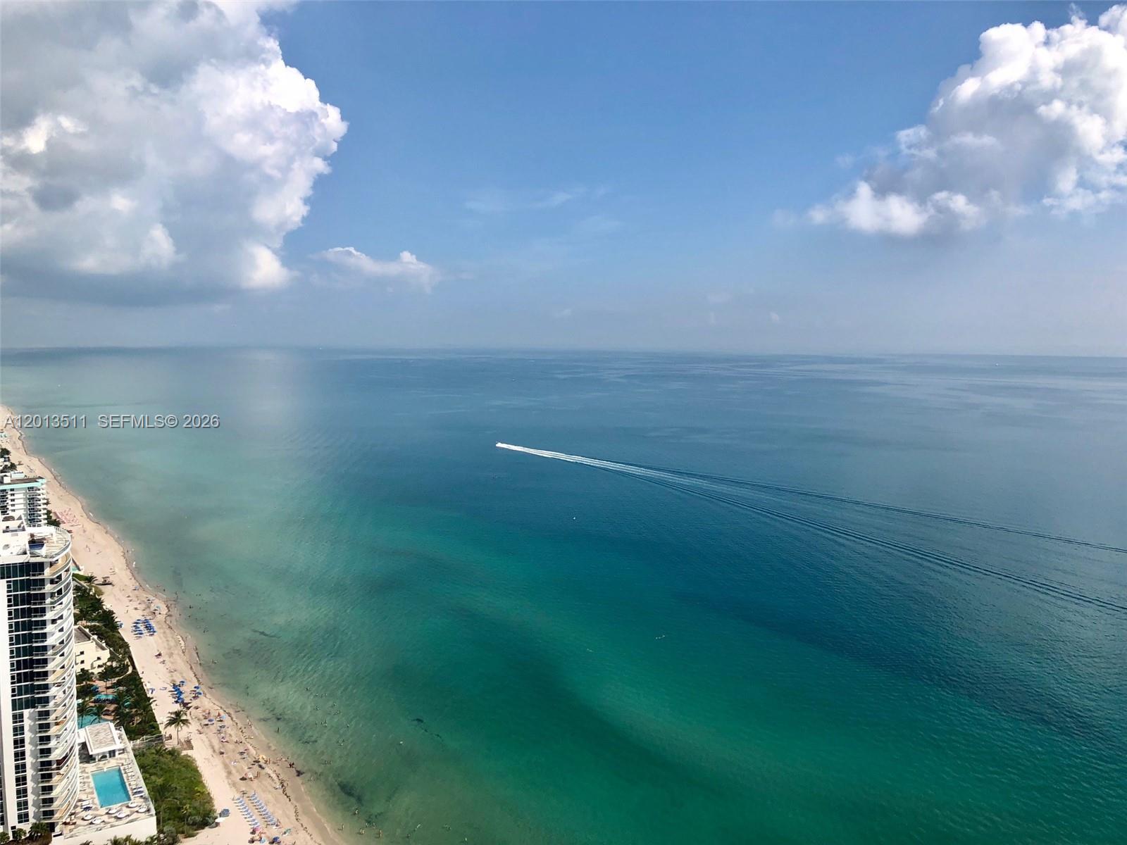 An aerial view shows a sandy beach, turquoise ocean, and a high-rise building — HALLANDALE BEACH, FL