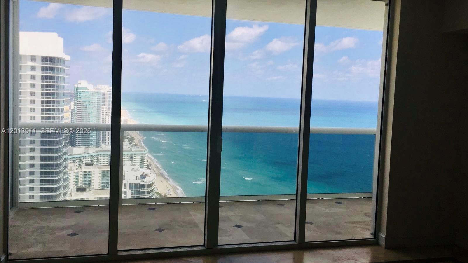 A view of the ocean and coastline from a high-rise balcony through floor-to-ceiling windows — HALLANDALE BEACH, FL