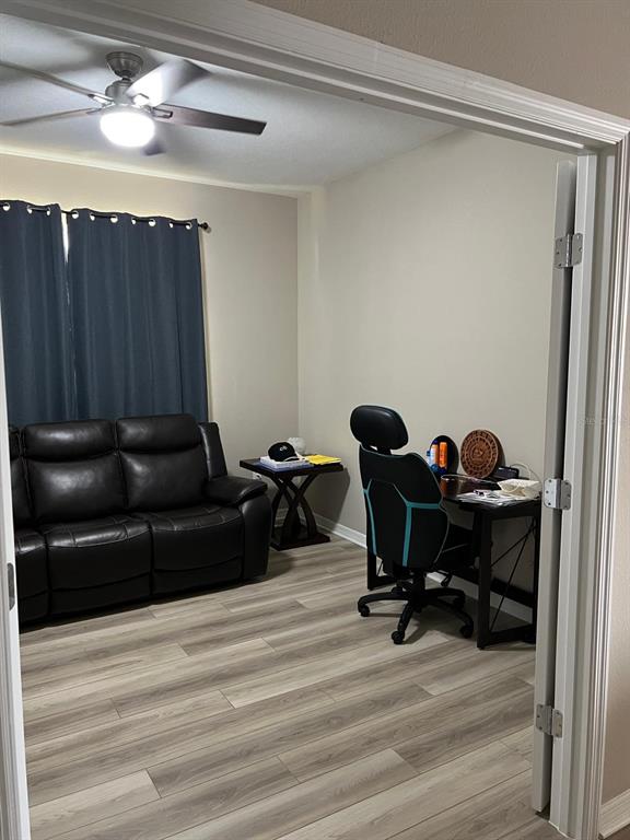 A room with wood-look flooring, a black leather sofa, a desk, and a ceiling fan — 3900 ALMOND BROOK BOULEVARD, LAND O LAKES, FL