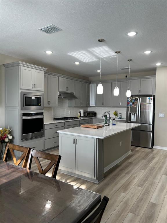 A kitchen features gray cabinetry, stainless steel appliances, a central island, and light wood flooring — 3900 ALMOND BROOK BOULEVARD, LAND O LAKES, FL