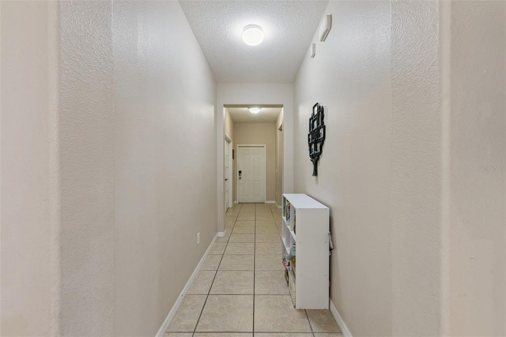 A tiled hallway leads to a white front door with a small bookshelf on the right — 1916 RUCKMAN PLACE, APOPKA, FL
