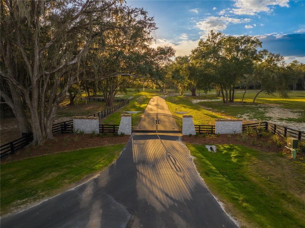 An aerial view shows a paved driveway leading to a gated entrance with stone pillars — 17197 SW 11 COURT, NEWBERRY, FL