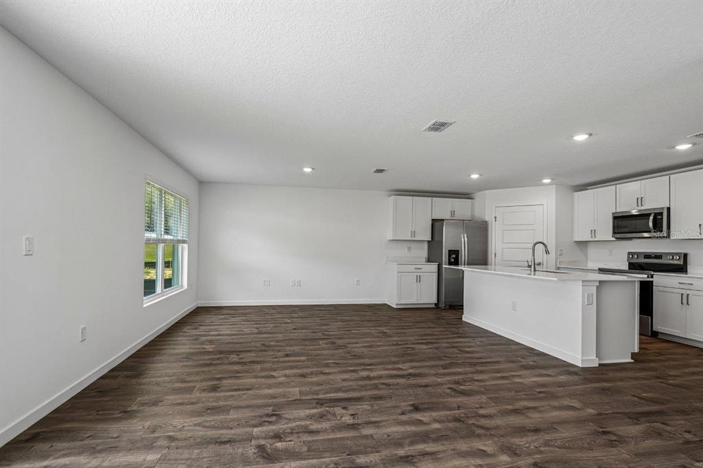 An open-concept kitchen and living area featuring white cabinets, stainless appliances, and wood-look flooring — 234 BULL FROG LANE, UMATILLA, FL