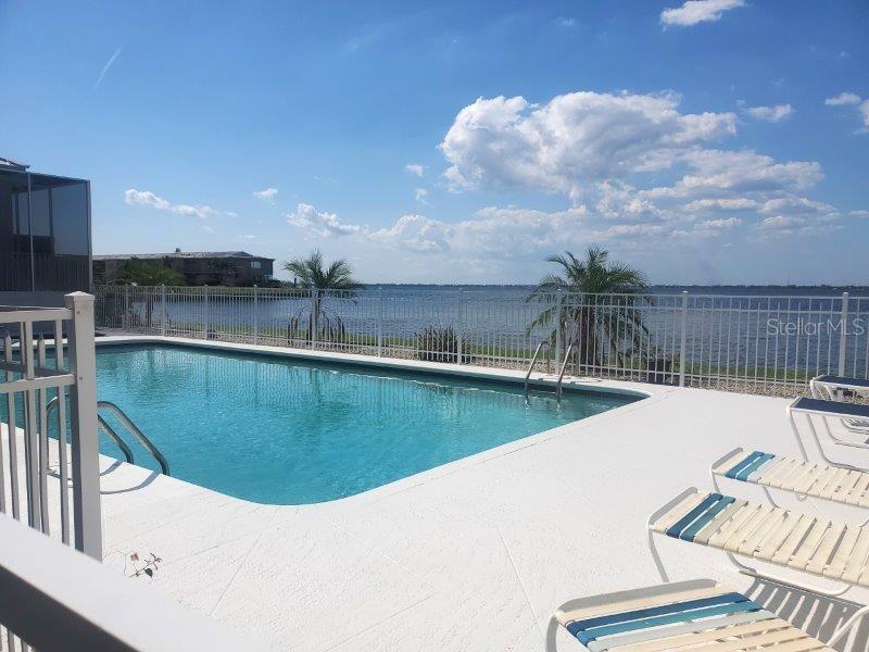 A swimming pool with lounge chairs overlooks a large body of water under a sky — 1600 W MARION AVENUE UNIT 232, PUNTA GORDA, FL