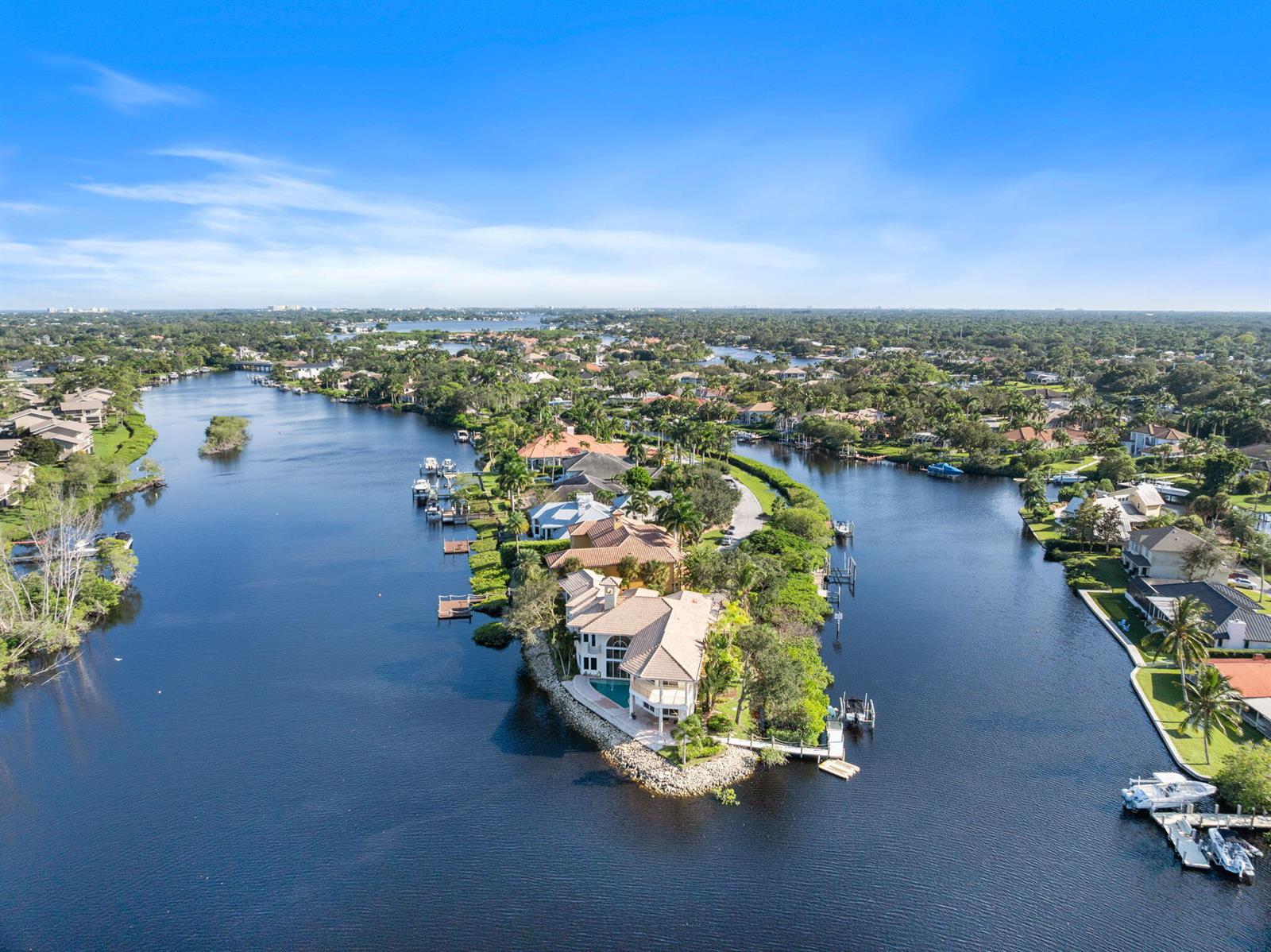 An aerial view shows a waterfront house on a peninsula surrounded by a canal — 18499 SE Palm Island Lane, Jupiter FL 33458, JUPITER, FL
