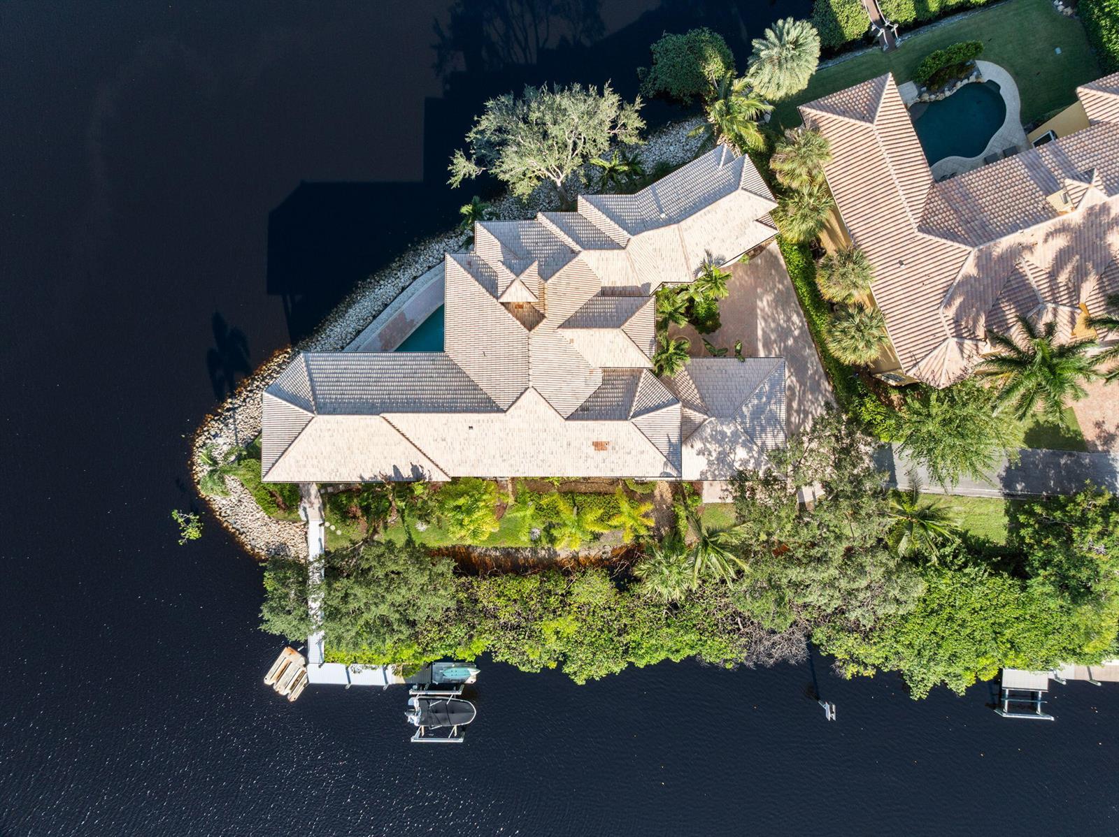An aerial view of a waterfront house with a tiled roof, pool, and private dock — 18499 SE Palm Island Lane, Jupiter FL 33458, JUPITER, FL