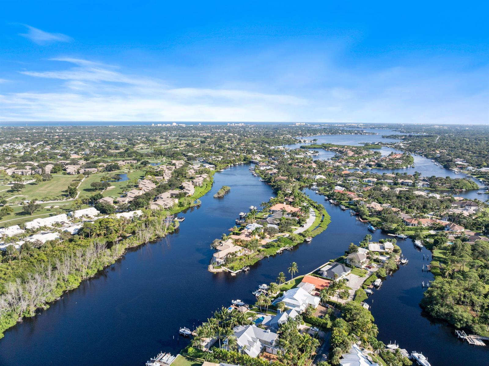 Aerial view of waterfront homes along a winding river surrounded by lush green landscapes — 18499 SE Palm Island Lane, Jupiter FL 33458, JUPITER, FL