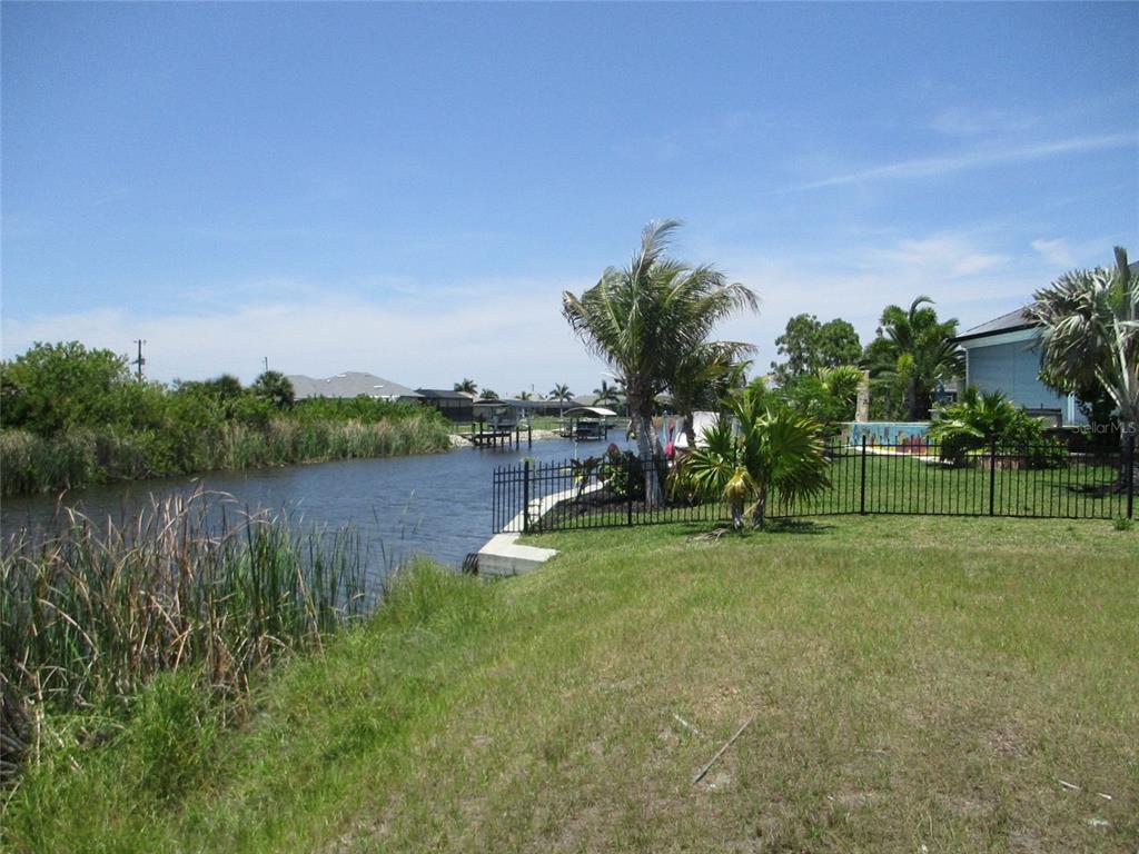 A grassy backyard overlooks a canal with a black metal fence and palm trees — 14478 LILLIAN CIRCLE, PORT CHARLOTTE, FL